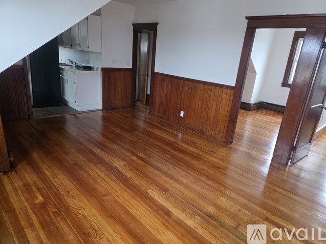 A room with wooden floors and a kitchen area in the background.