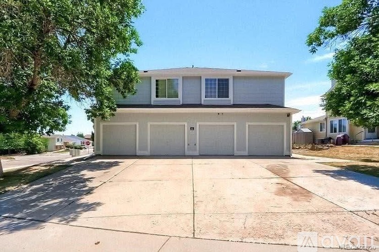 A two-story house with a garage is surrounded by trees and has a driveway in front.