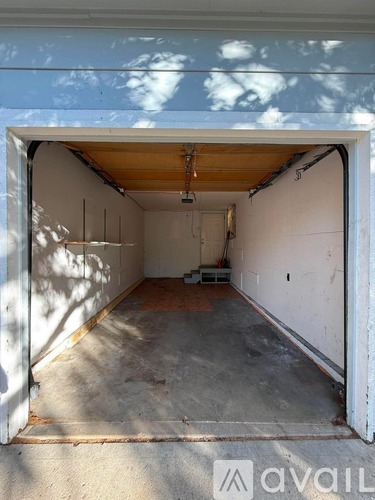 A large white garage door is open, revealing a concrete floor and a wall with some electrical wiring.