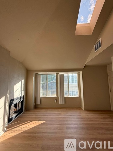 A spacious room with a skylight and a large window with blinds.