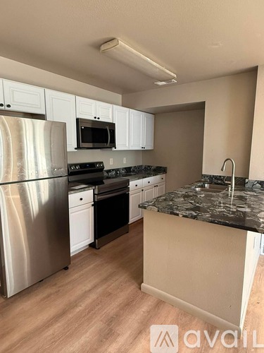 A kitchen with a stainless steel refrigerator, black countertops, and white cabinets.