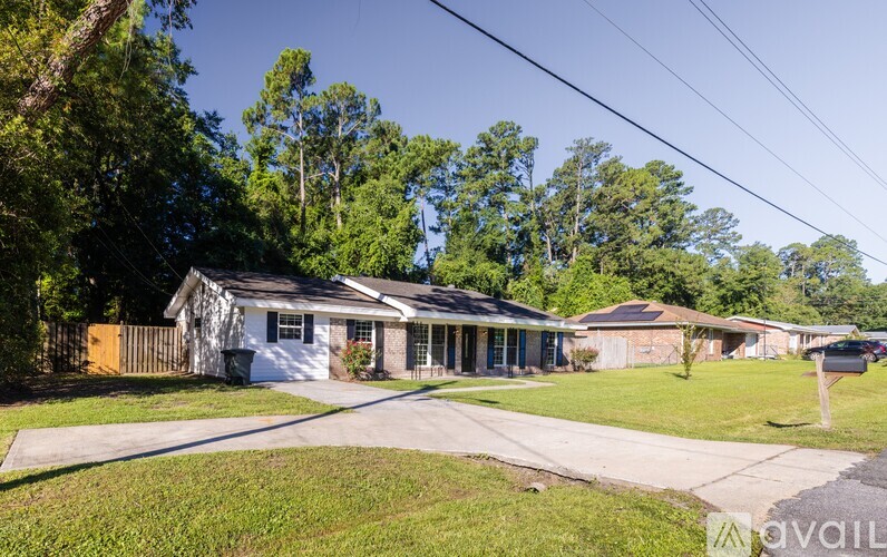 A house with a white exterior is surrounded by greenery and has a driveway leading to the front door.
