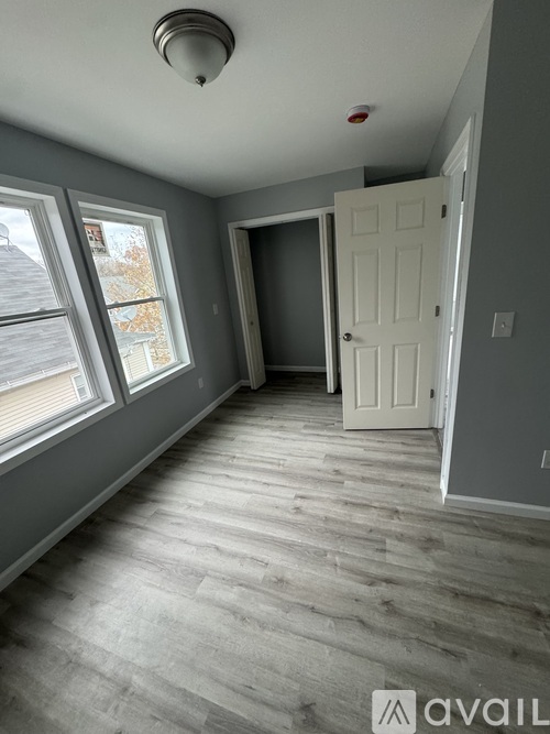 A room with a white door and a window with a view of a house across the street.