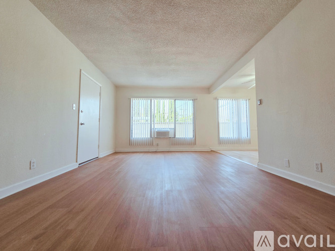 A spacious room with wooden floors and two windows.