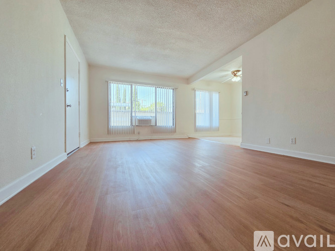 A spacious room with wooden flooring and large windows.