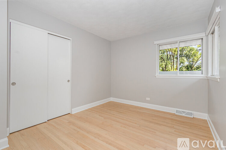 A room with a white door and a window with a view of trees outside.