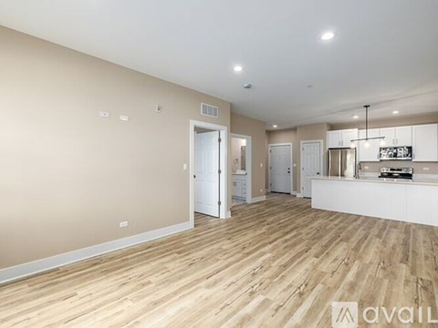 A spacious room with wooden flooring and a kitchen area in the background.
