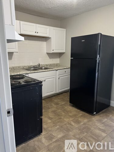 A black refrigerator stands in a kitchen with white cabinets and a black stove.