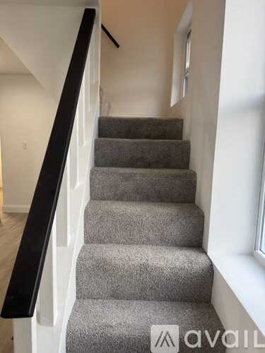 A staircase with a black railing and grey carpeted steps.