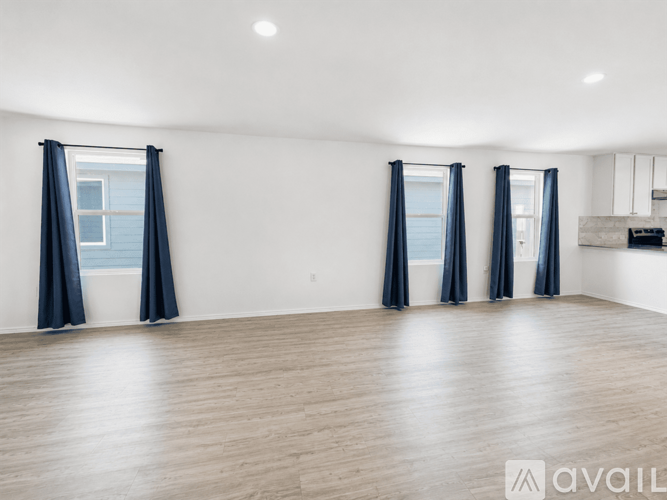 A spacious room with wooden flooring and three windows with blue curtains.