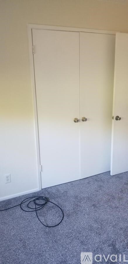 A white closet door with a black cord on the floor.