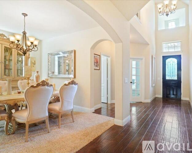 A large, elegant dining room with a chandelier, a dining table with chairs, and a view of a hallway.