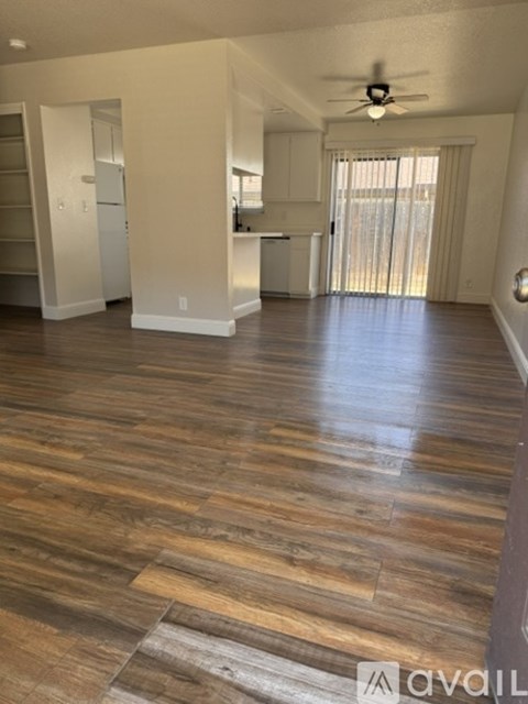 A living room with a ceiling fan and a kitchen in the background.