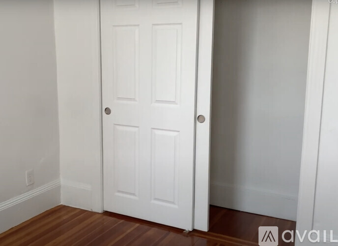 A white door with a silver handle is in a room with wooden floors.