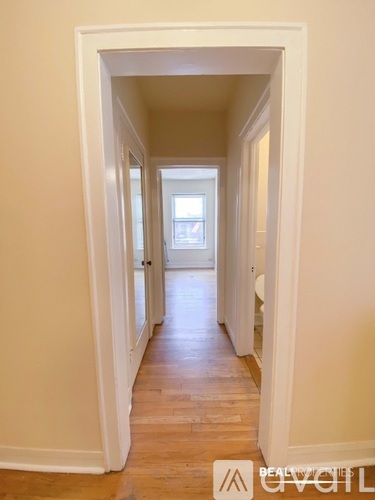 A hallway with a wooden floor and white walls leading to a door.