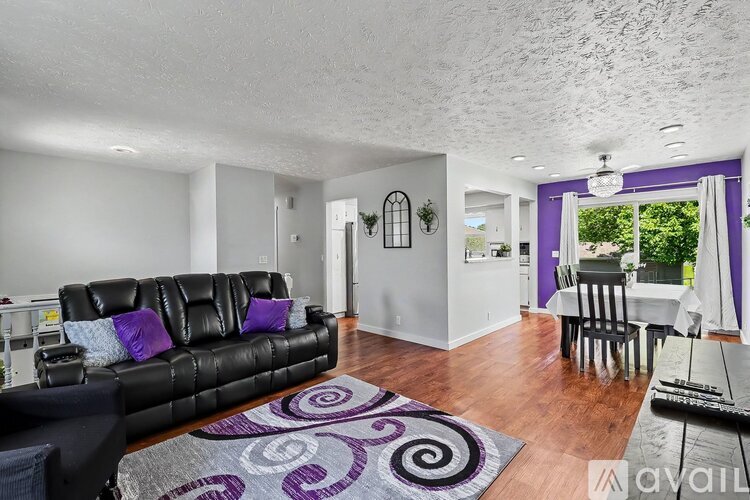A living room with a black leather couch and a purple rug.