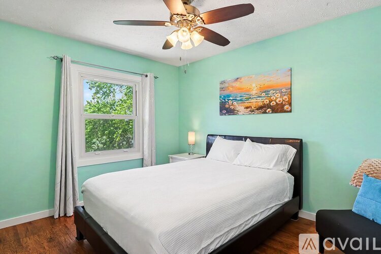 A bedroom with a bed, a ceiling fan, and a painting on the wall.
