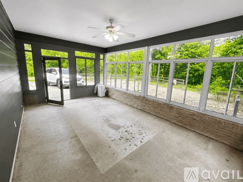 A room with a ceiling fan and a view of trees outside the windows.