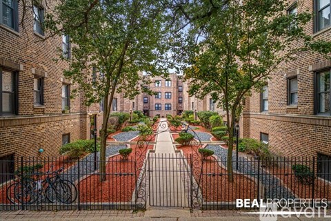 A BEALPROPERTIES sign is on a gate in front of a brick building.