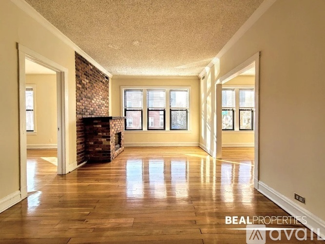 A spacious room with wooden floors and a brick fireplace.