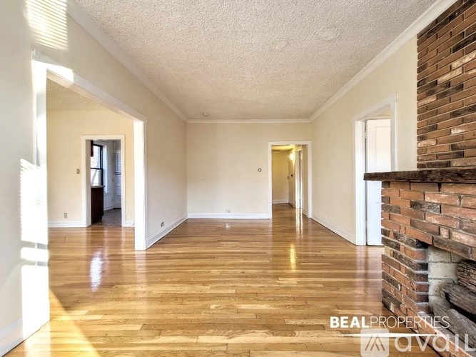 A spacious room with wooden flooring and a brick wall on the side.