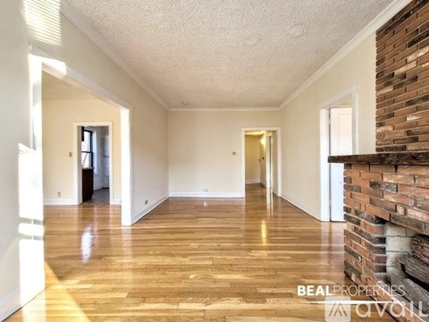 A spacious room with wooden flooring and a brick wall on the side.