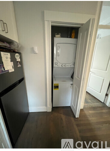 A small white washing machine is in a doorway between a kitchen and a laundry room.
