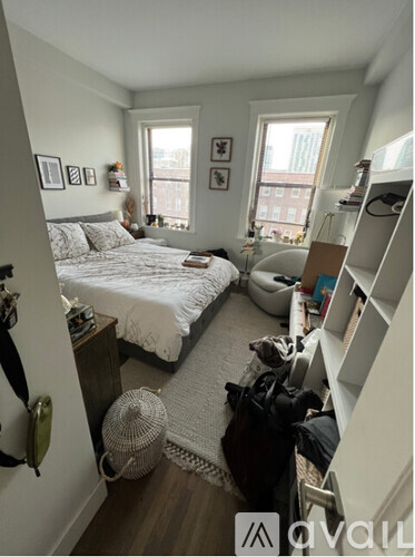 A bedroom with a bed, a fan, a window, and a shelf.