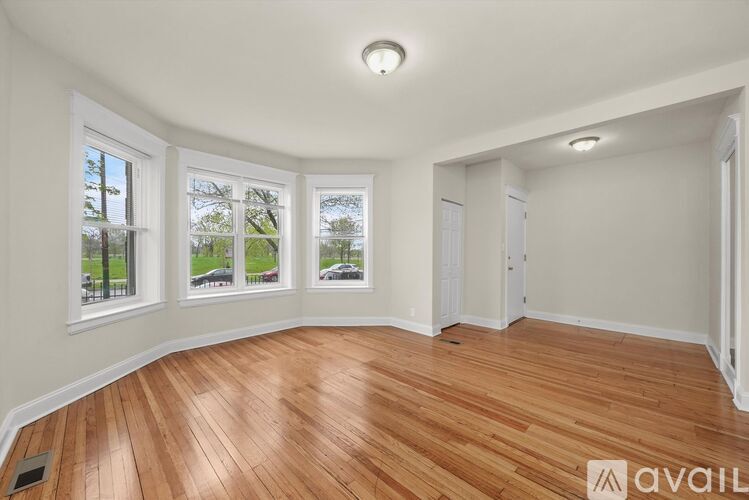 A room with wooden flooring and three windows overlooking a green area.
