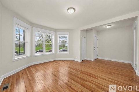 A room with wooden flooring and three windows overlooking a green area.