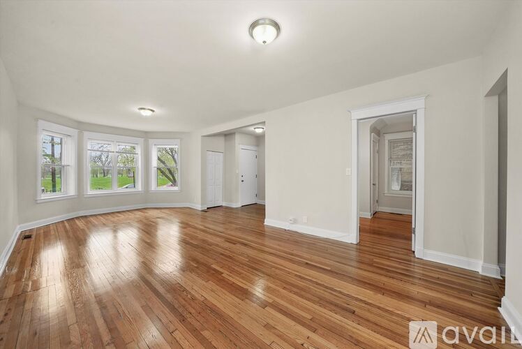 A room with wooden floors and white walls, with a window showing greenery outside.