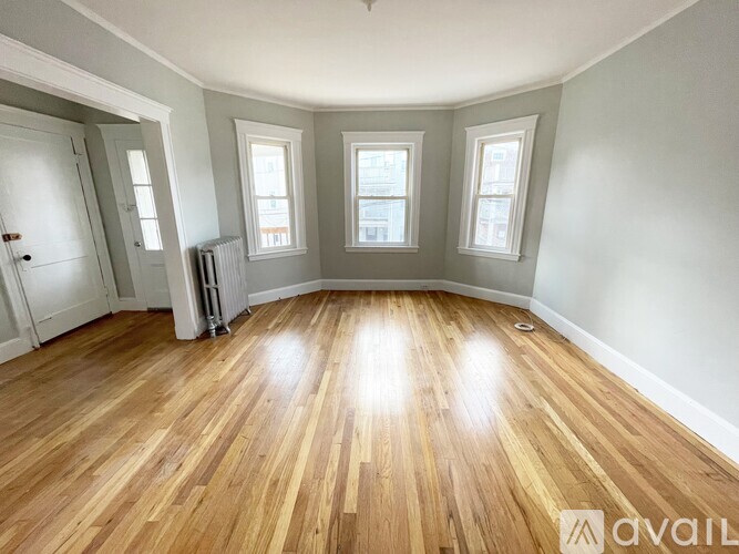 A room with wooden flooring and three windows.