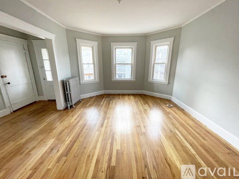 A room with wooden flooring and three windows.