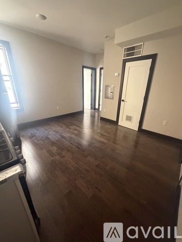 A room with wooden floors and white walls, with a window on the left side.
