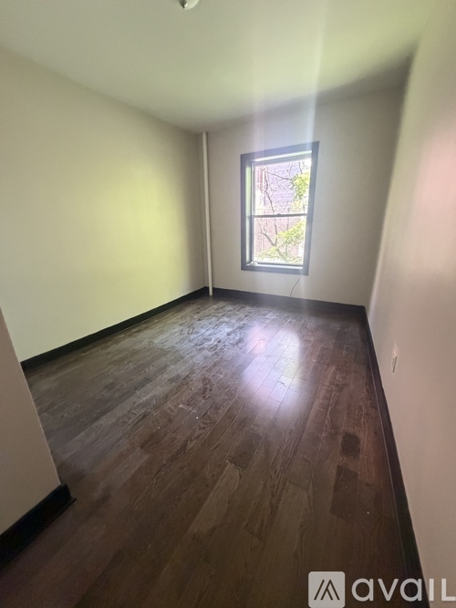 A room with wooden flooring and a window showing a tree outside.