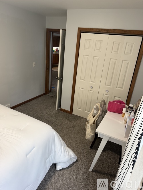 A bedroom with a white bed and a white desk with a pink bag on it.