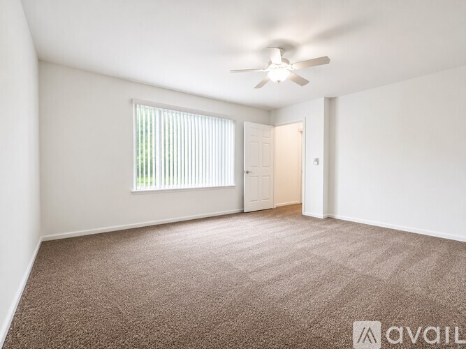 A room with a carpeted floor, a ceiling fan, and a window with blinds.