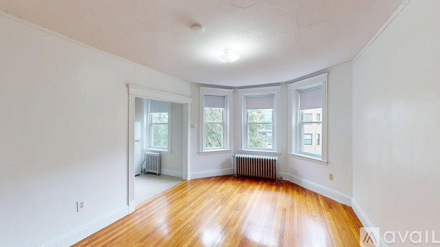 A room with wooden floors and white walls, with three windows and a radiator.