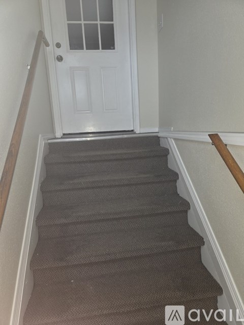 A staircase with a carpeted runner and wooden handrail leading to a white door.