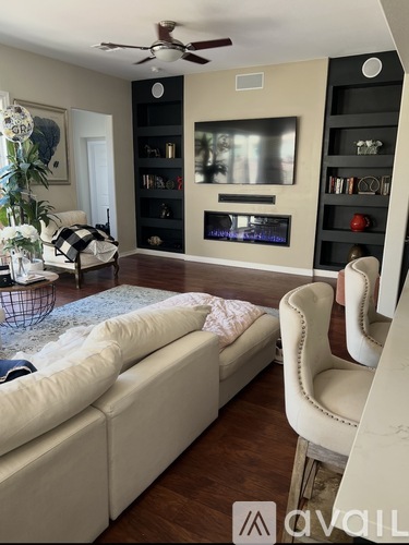 A living room with a white couch and a television on a black shelf.