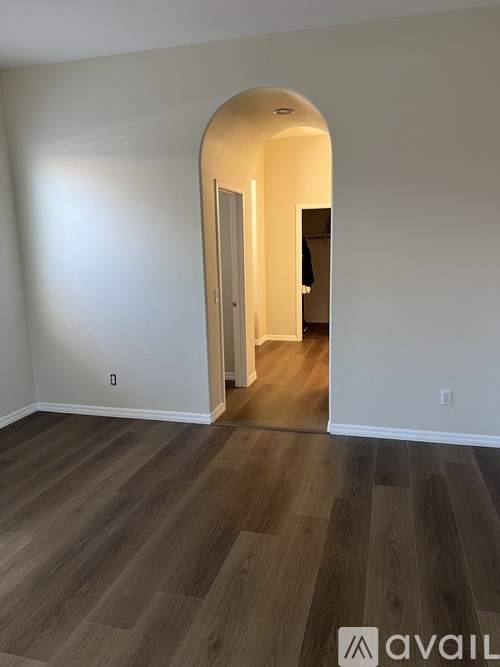 A room with a wooden floor and a white wall with a doorway leading to another room.