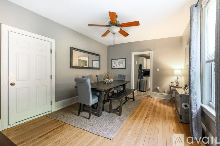 A room with a dining table and chairs, a ceiling fan, and a window with curtains.