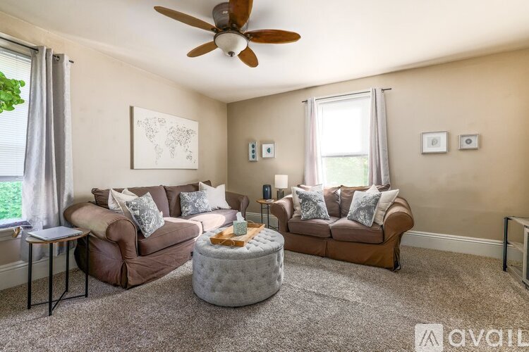 A living room with a brown couch, a grey ottoman, and a ceiling fan.