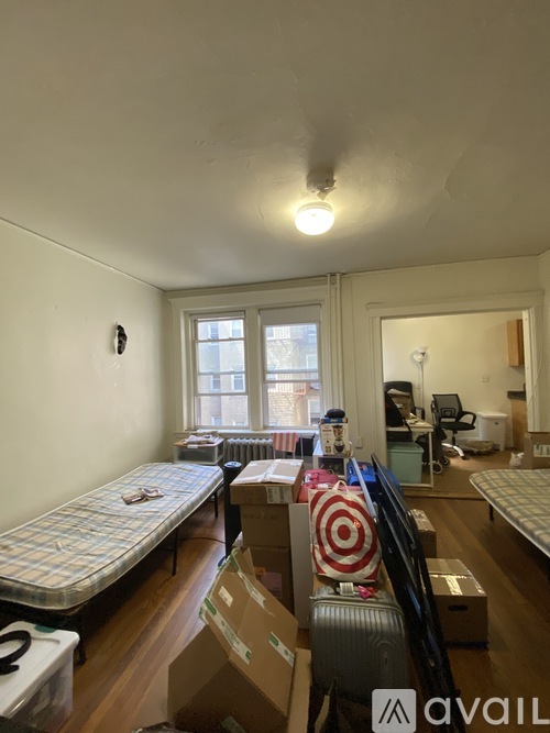A room with a bed, a chair, and a suitcase with a red and white design on it.