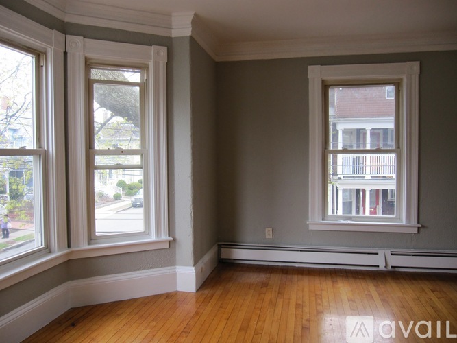 A room with two windows and wooden floors is available for rent.