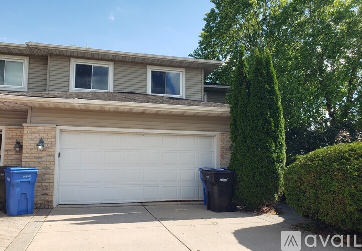 A house with a white garage door and a blue trash bin.