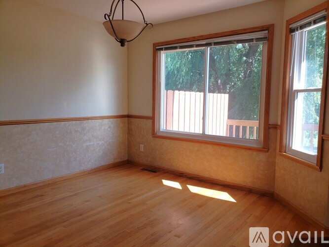 A room with wooden floors and a large window with a view of a fence and trees.