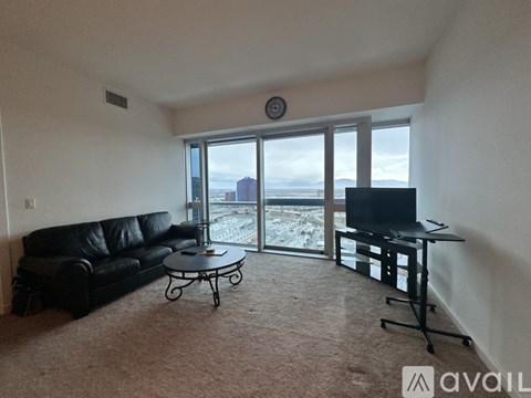 A living room with a black leather couch, a small round table, and a television set.