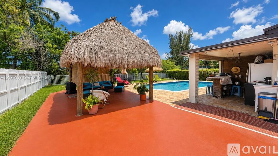A red patio area with a thatched roof and a pool in the background.