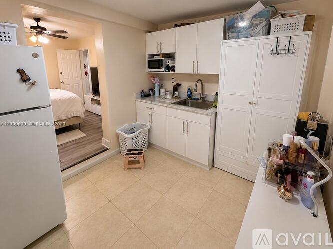 A kitchen with white cabinets and appliances, a bed, and a fan.